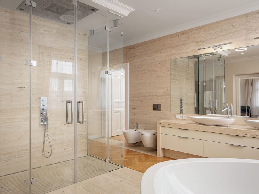 Un baño moderno con ducha envuelta en vidrio, una bañera independiente y un espejo grande sobre el lavabo.