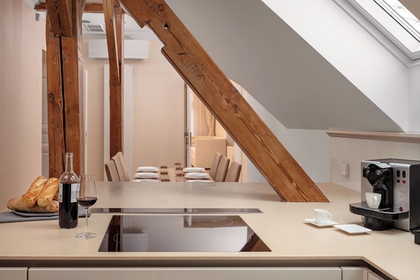 A modern kitchen with a large island, a coffee machine, and a dining area with a table set for two. - R16 Residences Prague (Prague)