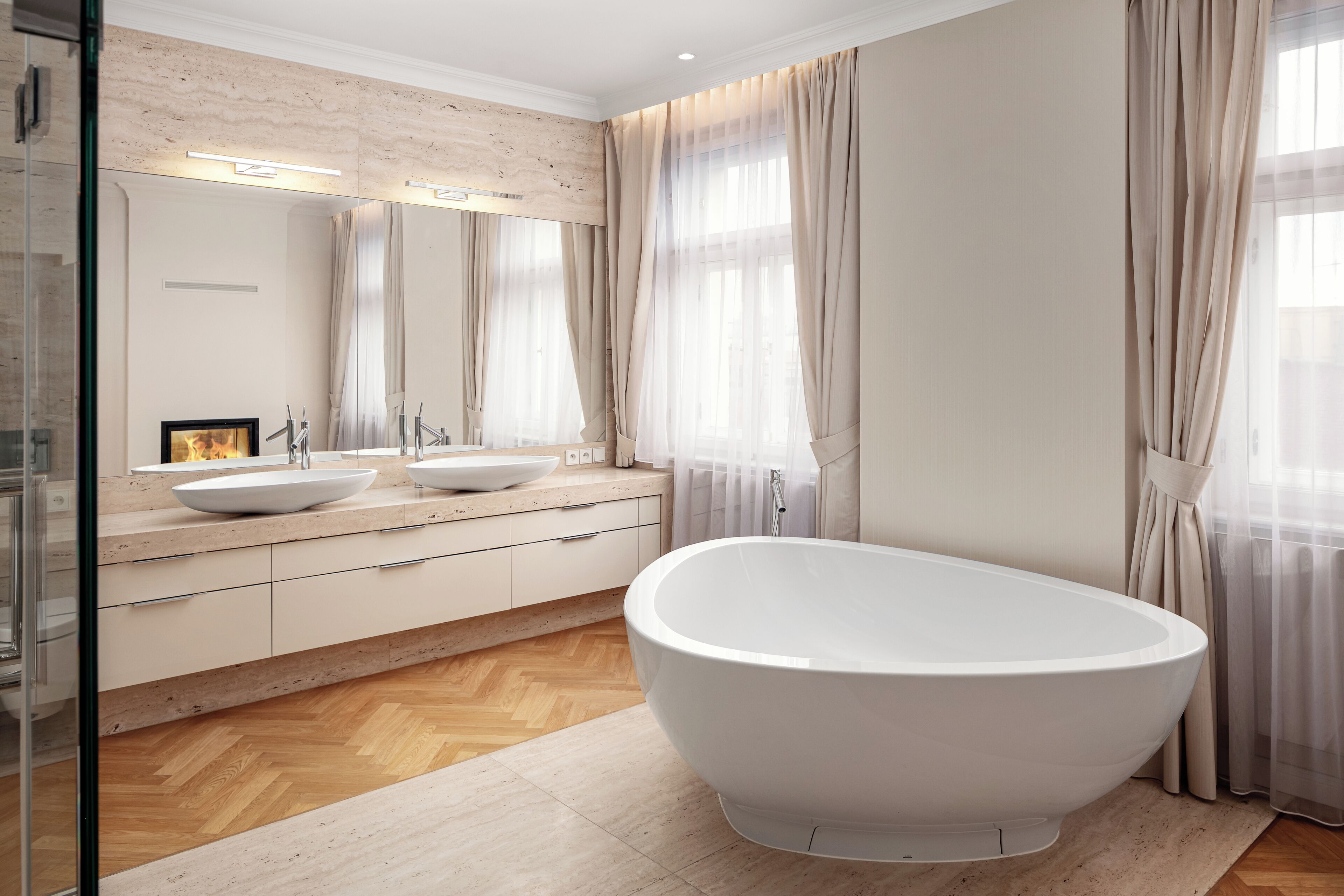 A modern bathroom with a freestanding bathtub, two sinks, and a large mirror.