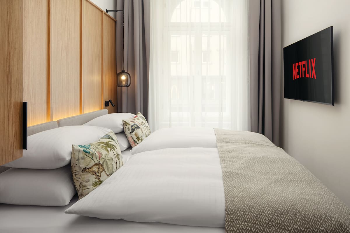 Un dormitorio moderno con una cama grande, un televisor montado que muestra 'NETFLIX' y una ventana con cortinas.