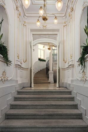 Una majestuosa escalera con detalles en oro ornamentados y un candelabro.