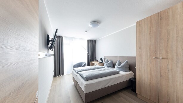 A modern bedroom with a bed, bedside tables, a wardrobe, and a mirror. - Centerroom München City (Munich)