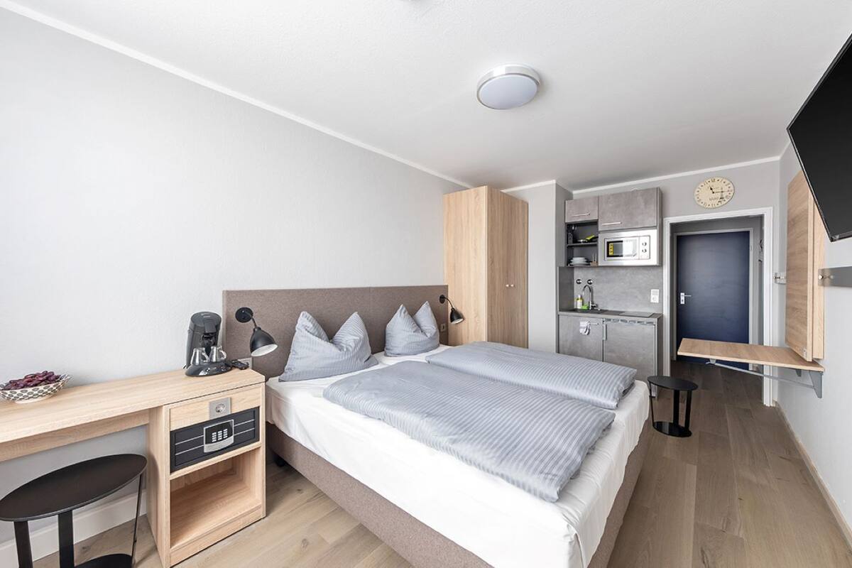 Une chambre d’hôtel moderne équipée d’un lit, d’un bureau, d’une chaise, d’une petite table, d’un four à micro-ondes et d’une télévision.