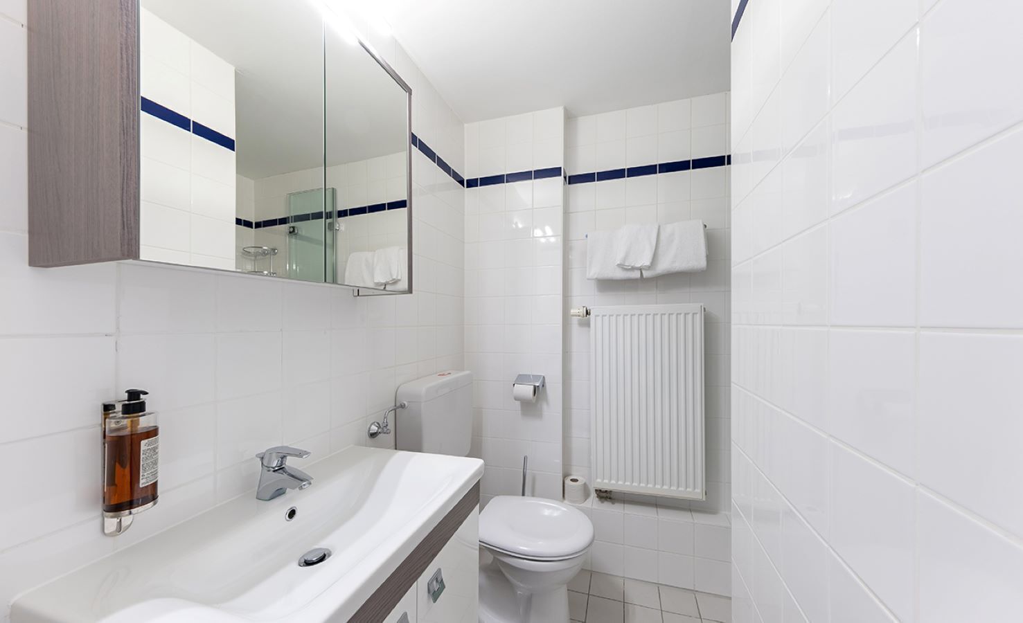 A modern bathroom with a white sink, mirror, and toilet. There is a glass shower enclosure and a towel rack with towels.