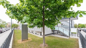 Edifici modern amb una escala que condueix a un nivell superior, envoltat d'una zona d'aparcament i un arbre.