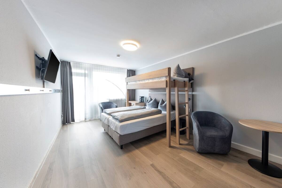 Une chambre d’hôtel moderne équipée d’un lit superposé, d’un bureau, d’une chaise et d’une petite table.