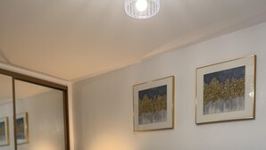 Een net opgemaakt bed met een gebreid plaid, een bedlampje en een ingelijst plaatje aan de muur.
