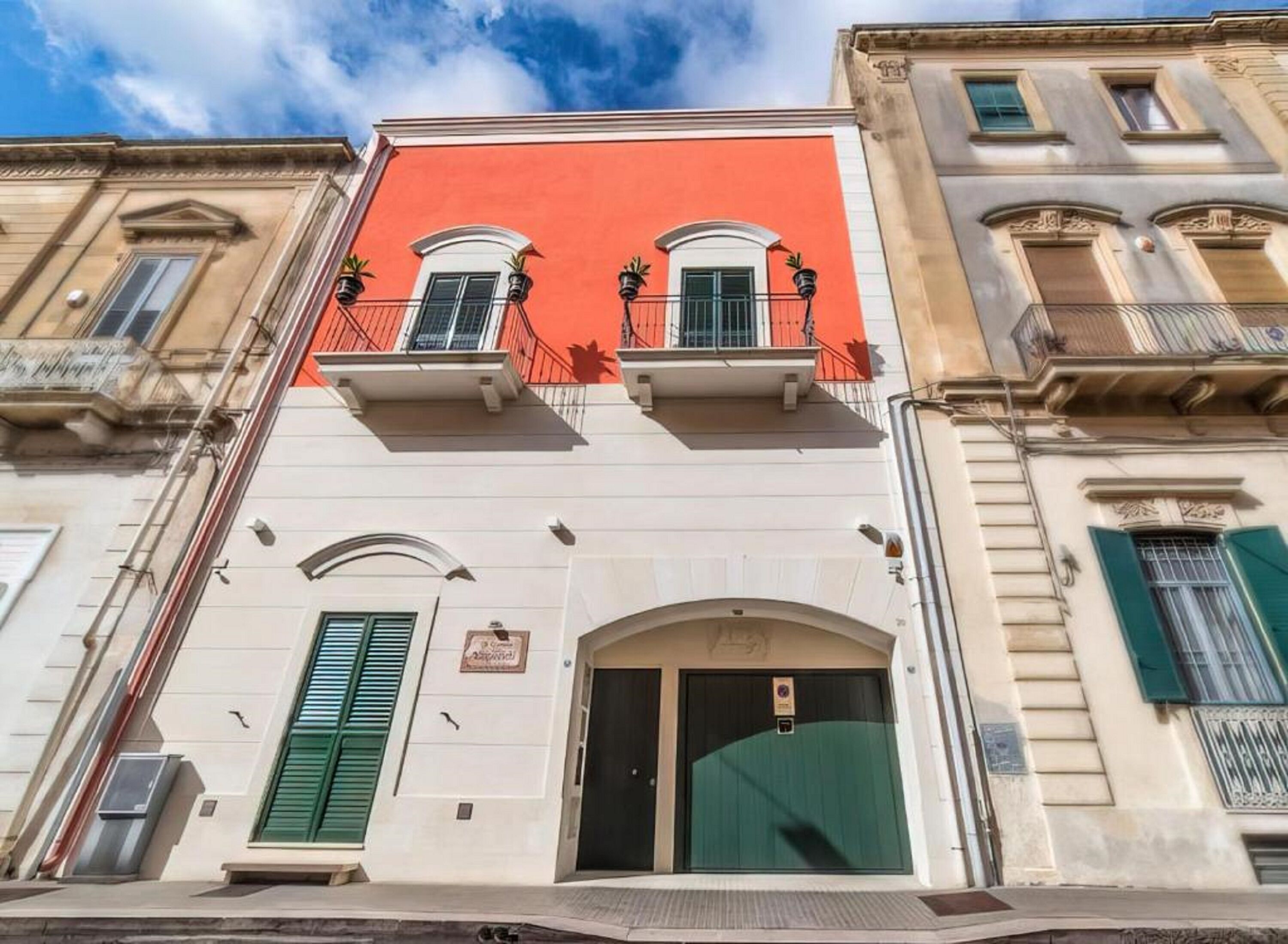 Un bâtiment à la façade rouge, aux étages supérieurs blancs et aux volets verts.