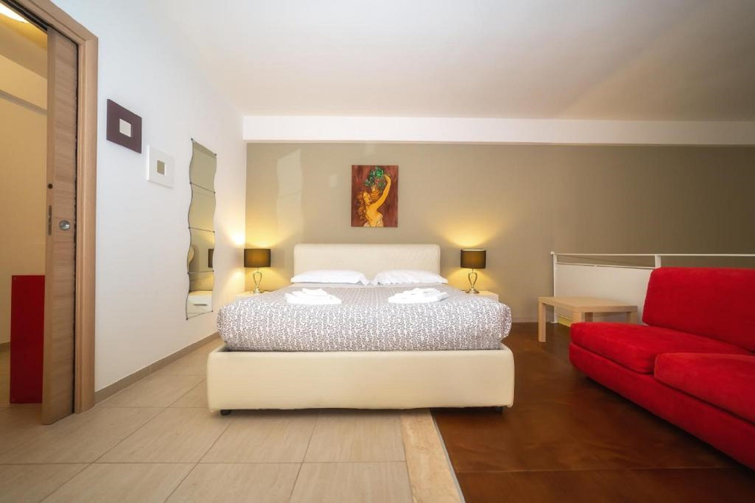 A bedroom with a bed, bedside lamps, a red sofa, and a painting on the wall.