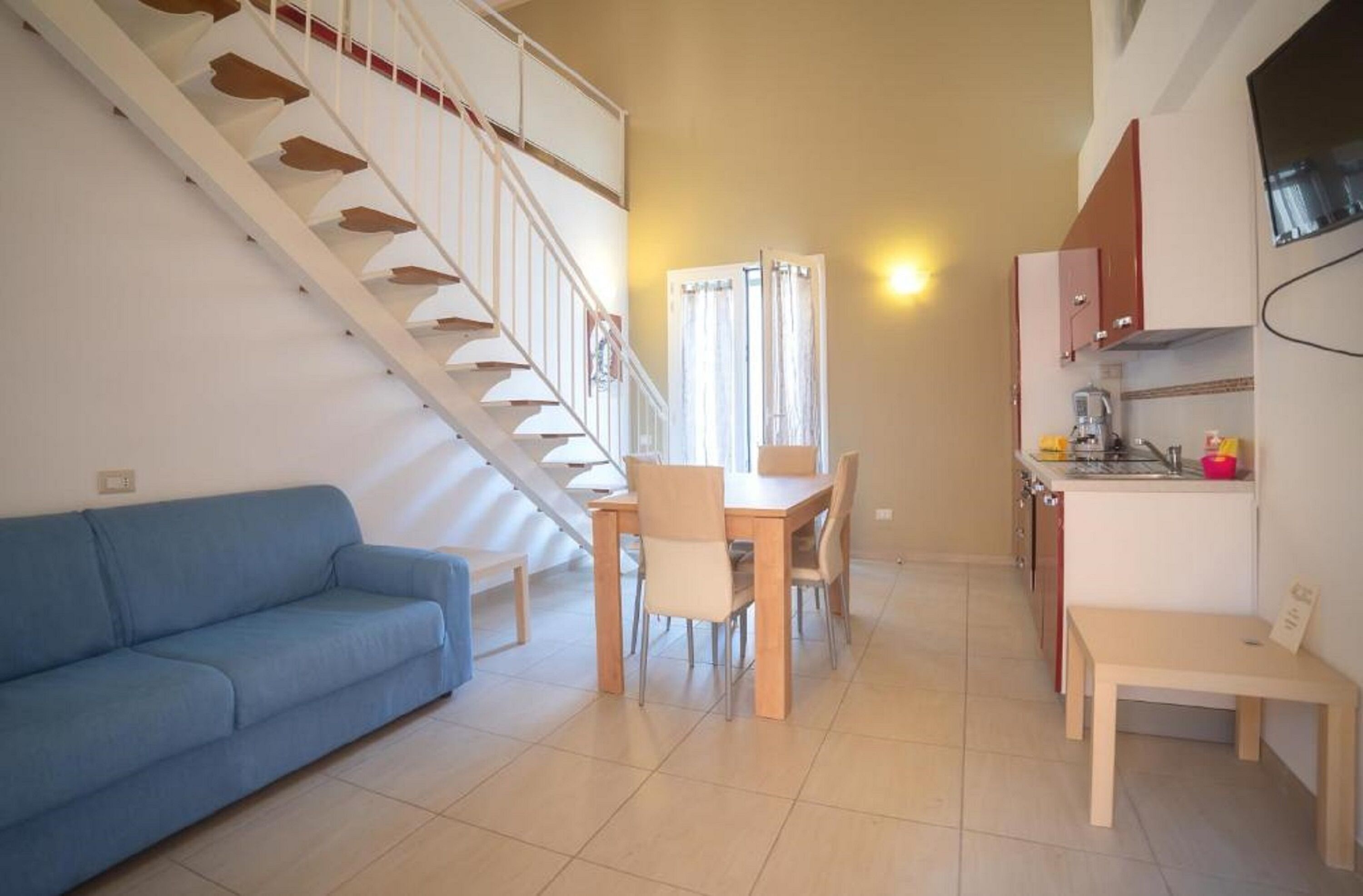 A compact living space with a staircase, a dining area, a kitchenette, and a blue sofa.