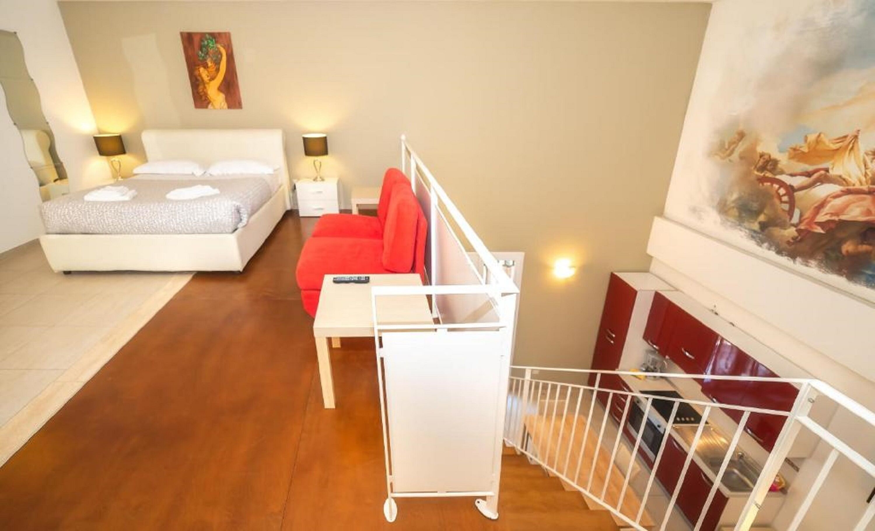A bedroom with a bed, a red chair, a small table, and a white railing.