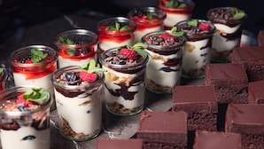 Une variété de desserts présentés dans des pots en verre, notamment des parfaits à plusieurs couches aux fruits rouges et au chocolat, ainsi que des carrés de chocolat servis à part.