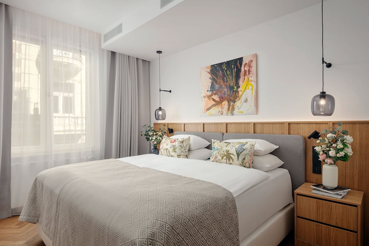 Une chambre d’hôtel moderne avec un grand lit, une tête de lit en bois, un tableau au mur et une table de chevet agrémentée d’un vase de fleurs.