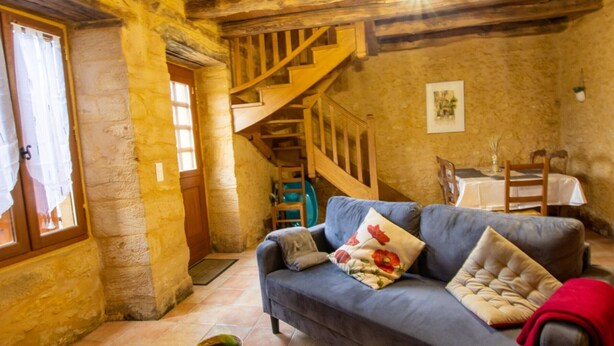 Ein rustikales Interieur mit einer Holztreppe, einem blauen Sofa mit Kissen und einem Essbereich mit Tisch und Stühlen.