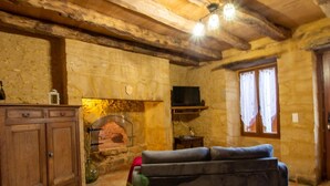Ein rustikaler Raum mit freiliegenden Holzbalken, einem Kamin aus Stein, einem Fernseher und einem Sofa.