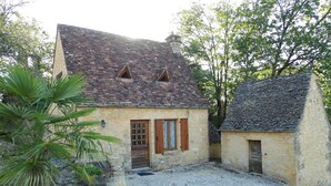 Ein rustikales Steinhaus mit geneigtem Dach, einer kleinen Veranda und einer Schotterauffahrt.