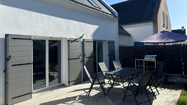 Une terrasse avec une table et des chaises, une porte-fenêtre coulissante et un espace abrité avec un parasol.