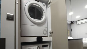 A compact laundry room with a front-loading washing machine and a top-loading dryer, both in a modern design. - "Dione" Luxury Business Suite in the Heart of Athens (Athina)