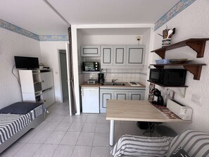 Eine kompakte Küche mit Mikrowelle, Toaster und Kaffeemaschine. Es gibt einen kleinen Kühlschrank und einen Esstisch mit einem Stuhl.
