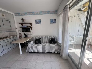 A compact kitchen with a dining area, a sofa, and a view through a glass door.