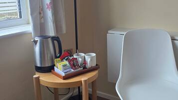 Une pièce avec une table en bois, une chaise blanche, un lampadaire, un radiateur et une fenêtre avec des stores.