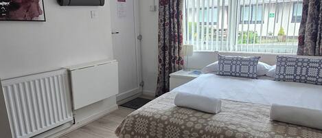 A bedroom with a bed, a radiator, a window with curtains, and a wall-mounted air conditioner.