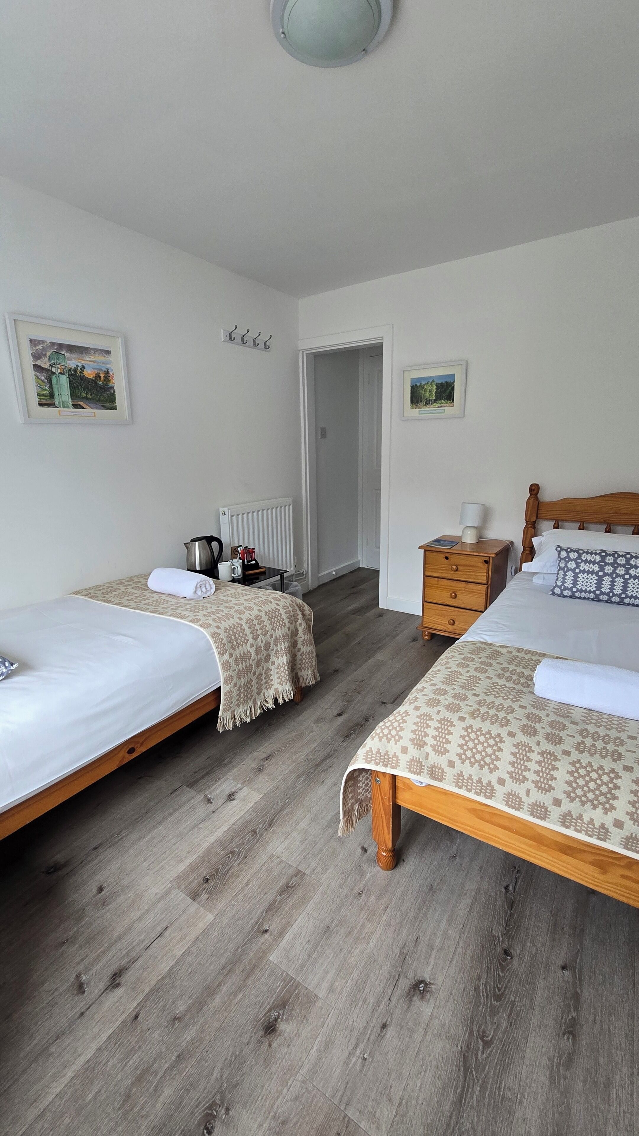 Una habitación con dos camas individuales, un aparador de madera, un radiador y una puerta que da a otra habitación.