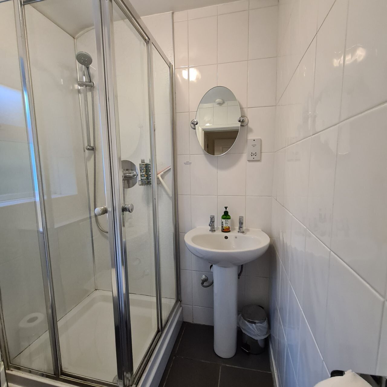 A bathroom with a glass-enclosed shower, a pedestal sink, and a mirror above the sink.