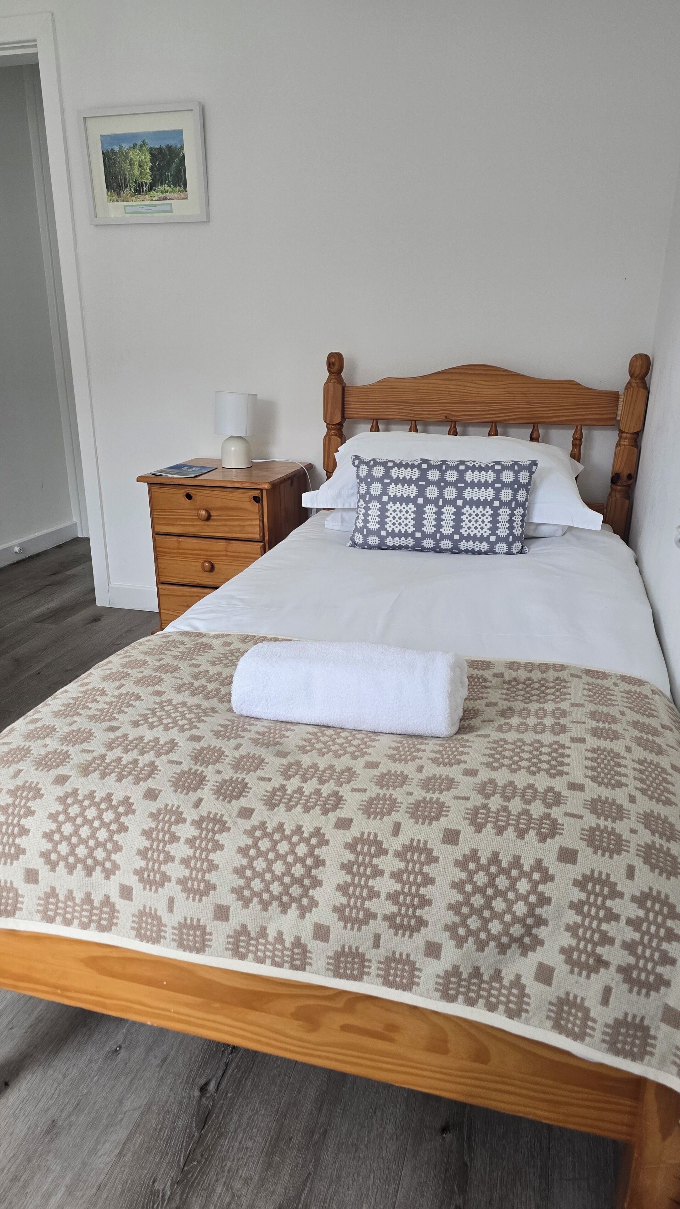 A neatly made bed with a patterned bedspread, a pillow with a geometric design, and a bedside table with a lamp.