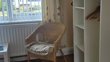 A room with a wicker chair, a white shelving unit, a radiator, and a window with blinds.