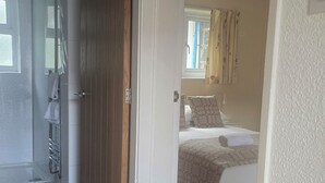 Una habitación con cama, ventana con cortinas, puerta que da a otra estancia y suelo de baldosas.