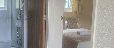 A room with a bed, a window with curtains, a door leading to another room, and a tiled floor.