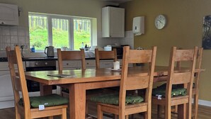 Un comedor con una mesa y sillas de madera, una cocina al fondo y un reloj en la pared.