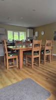 Un comedor con una mesa y sillas de madera, una cocina al fondo y un reloj en la pared.