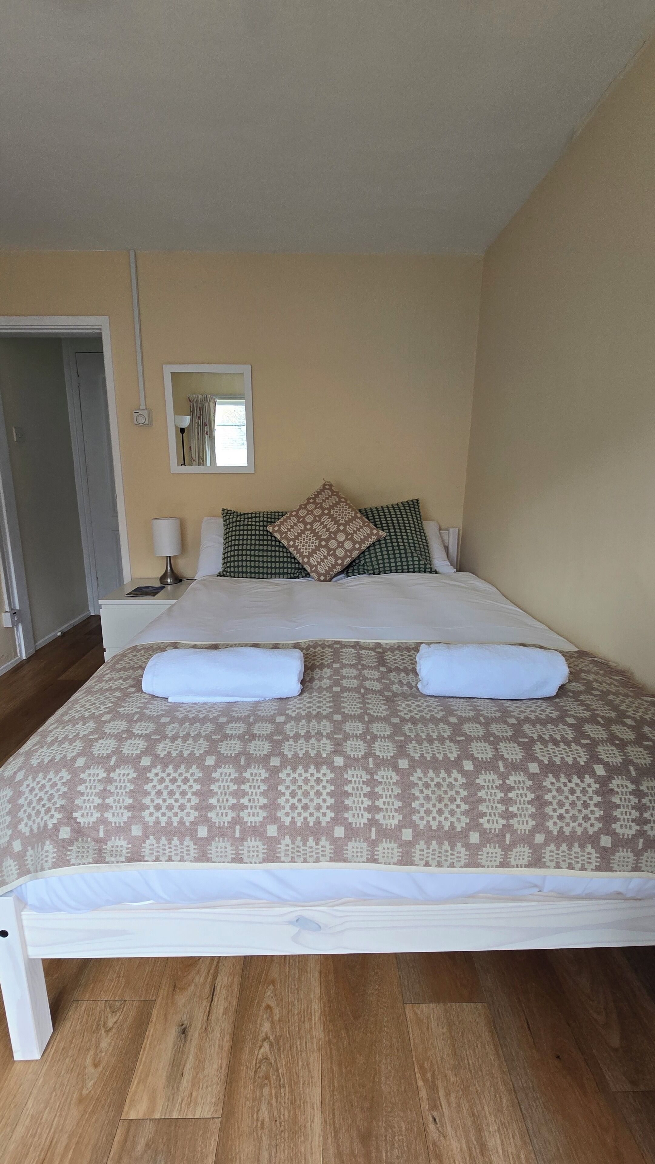 A neatly made bed with patterned bedding, a bedside lamp, and a window with curtains.