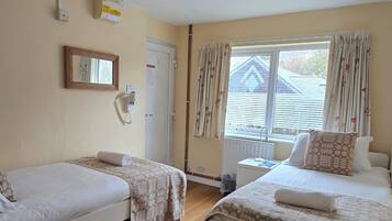A hotel room with two beds, a window with curtains, a radiator, and a wall-mounted phone.
