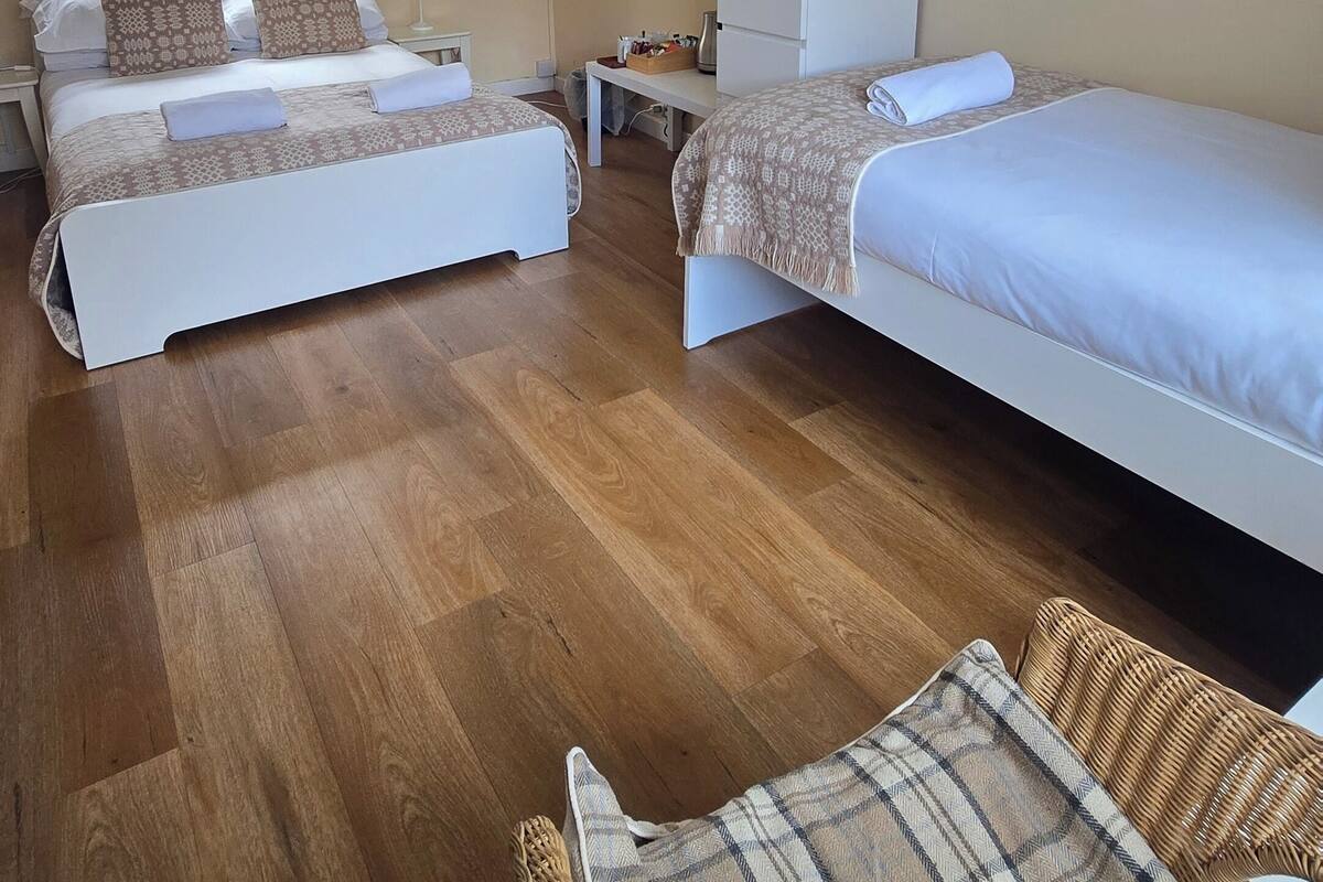 Habitación de hotel con dos camas, un escritorio pequeño, una silla, piso de madera y una ventana con cortinas.