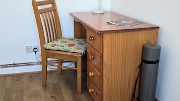 A wooden desk with a lamp, a chair, and a rolled-up mat.