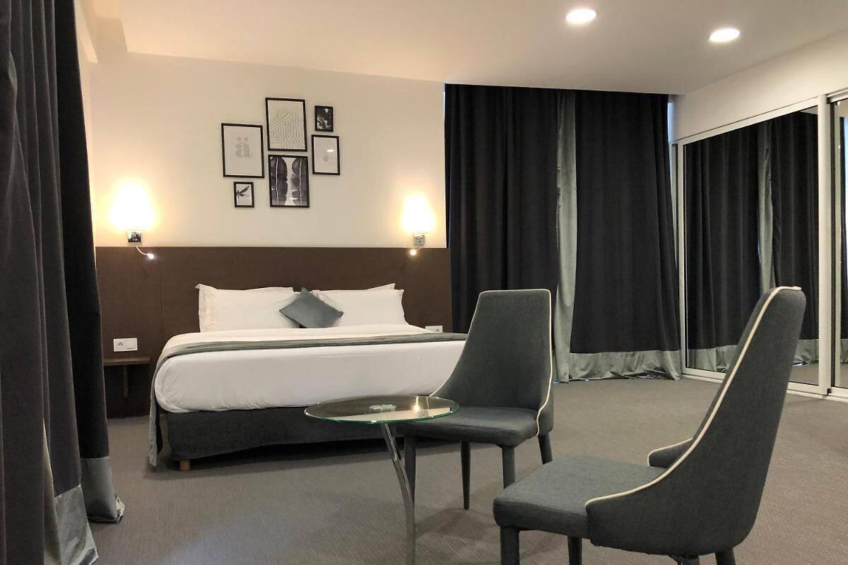 Une chambre d’hôtel avec un lit, deux chaises, une petite table et un mur orné de tableaux.