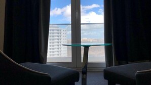 A room with a glass table and two chairs, a large window with a view of a cityscape and a building.