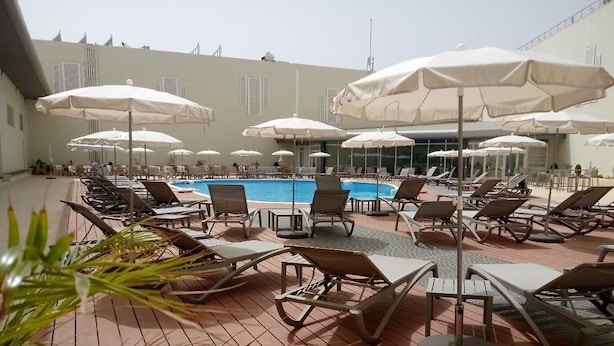 A poolside area with sun loungers and umbrellas, a pool, and a wooden deck.