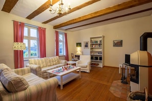 A cozy living room with a sofa, armchairs, a coffee table, a fireplace, and a bookshelf. - Altes Pastorat: Wohnung mit Kamin und Großem Garten (Borrentin)