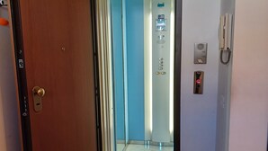 A hallway with a wooden door, an elevator, and a wall-mounted intercom. - Genius Home - Bright apartment in the heart of the historic center (Palermo)