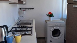 A compact kitchen with a gas stove, sink, and a small washing machine. - Genius Home - Bright apartment in the heart of the historic center (Palermo)