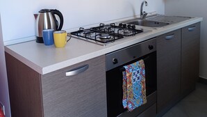 A modern kitchen with a gas stove, stainless steel appliances, and wooden cabinets. - Genius Home - Bright apartment in the heart of the historic center (Palermo)