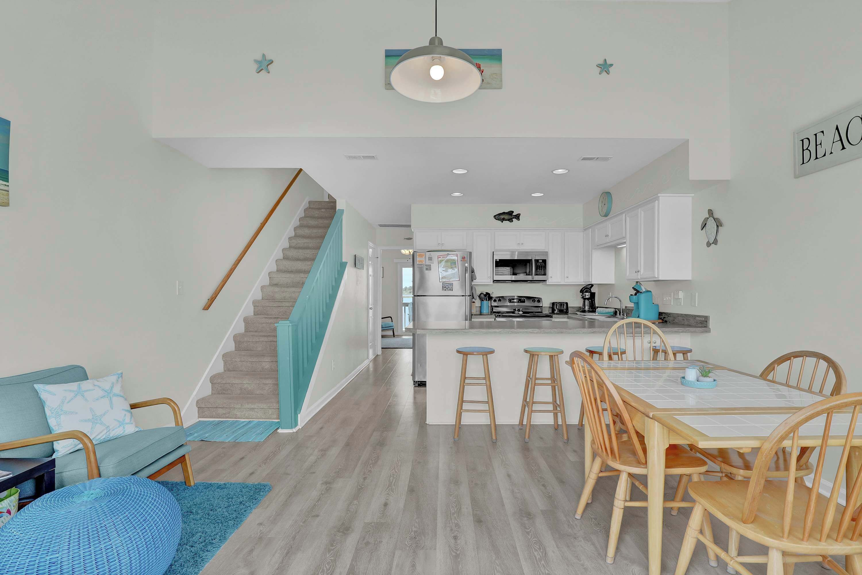 A modern kitchen with white cabinets, a central island, and a dining area with wooden chairs and stools.