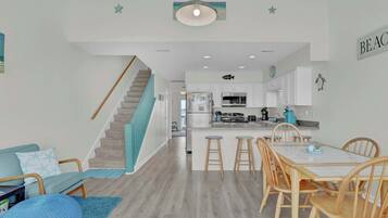 A modern kitchen with white cabinets, a central island, and a dining area with wooden chairs and stools.