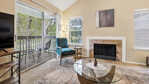 Una sala de estar con televisor, chimenea, un sillón azul y una mesa de centro de vidrio.