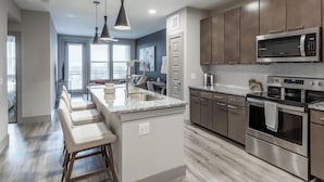 A modern kitchen with a central island, stainless steel appliances, and a bar seating area. - Landing | Stylish 1BD, Gym, Courtyard (Austin)