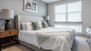 Quarto com uma cama, duas mesas de cabeceira, uma janela com persianas e um quadro na parede.